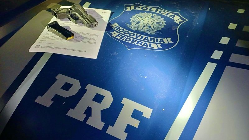 Pistola e munições apreendidas sobre capô de viatura da Polícia Rodoviária Federal