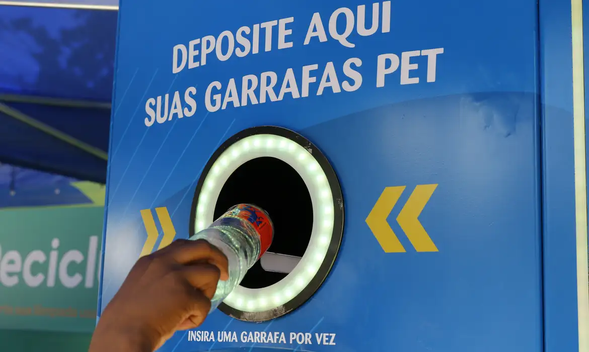 Mão deposita uma garrafa plástica em equipamento de coleta de embalagens PET; foto de arquivo, sem relação com os projetos selecionados.