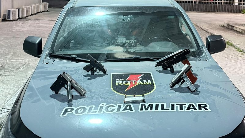 Quatro armas apreendidas são expostas sobre o capô de uma viatura da Rotam