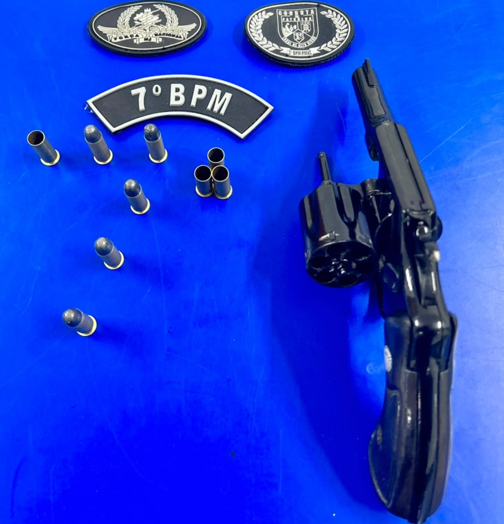 Revólver e munições sobre uma mesa azul, ao lado de identificações do 7º Batalhão da Polícia Militar de Alagoas.
