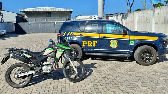 Motocicleta verde e preta apreendida ao lado de viatura da PRF em pátio, em foto divulgada em 15 de outubro de 2026.