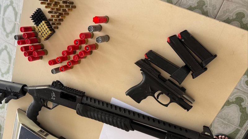 Espingarda, pistola, carregadores e munições apreendidos em ação policial em Arapiraca, sobre uma mesa.