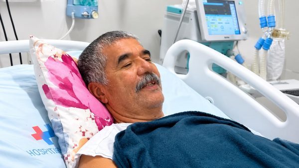 Aluízio Bernardo em leito hospitalar, fazendo sinal positivo com a mão após transplante hepático